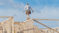 A man walking along the top beam of a shell house, a house you can build yourself.