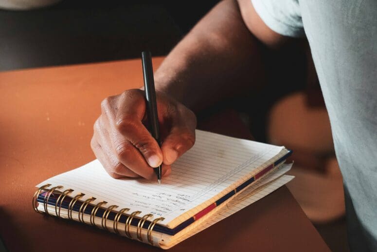 Anonymous man writing a to-do list in a white ruled paper notebook.