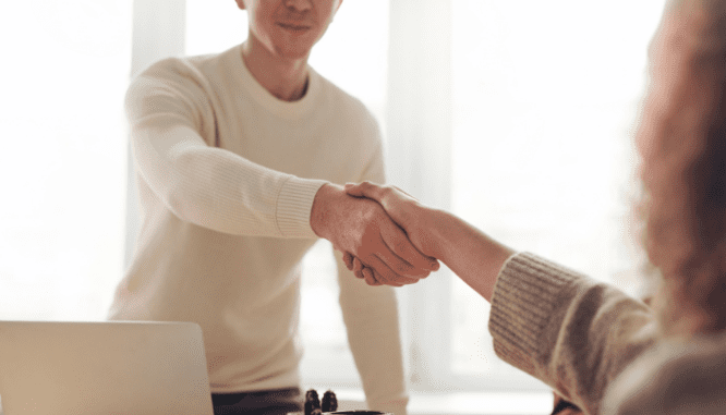 A seller shaking hands with a buyer over an offer.