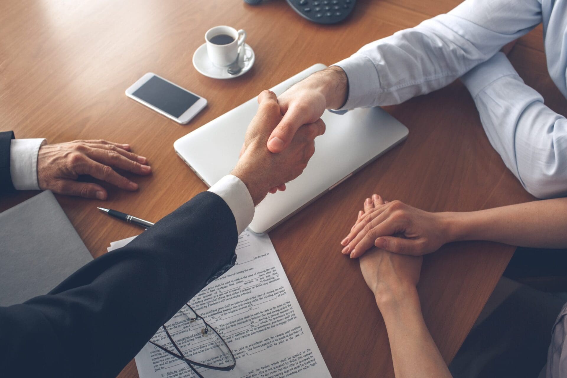 image of two people shaking hands over a contract and a laptop