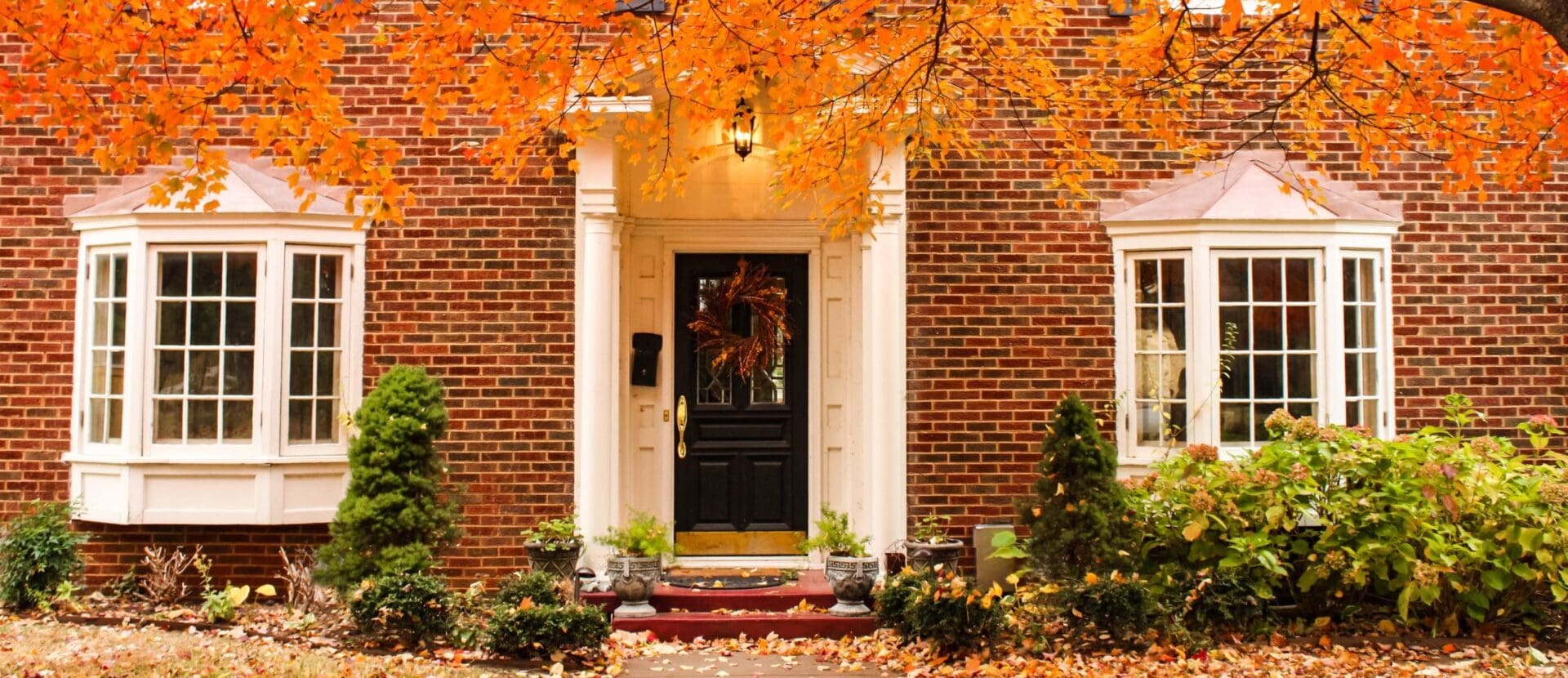 House in autumn with red brick, black door, and orange leaves