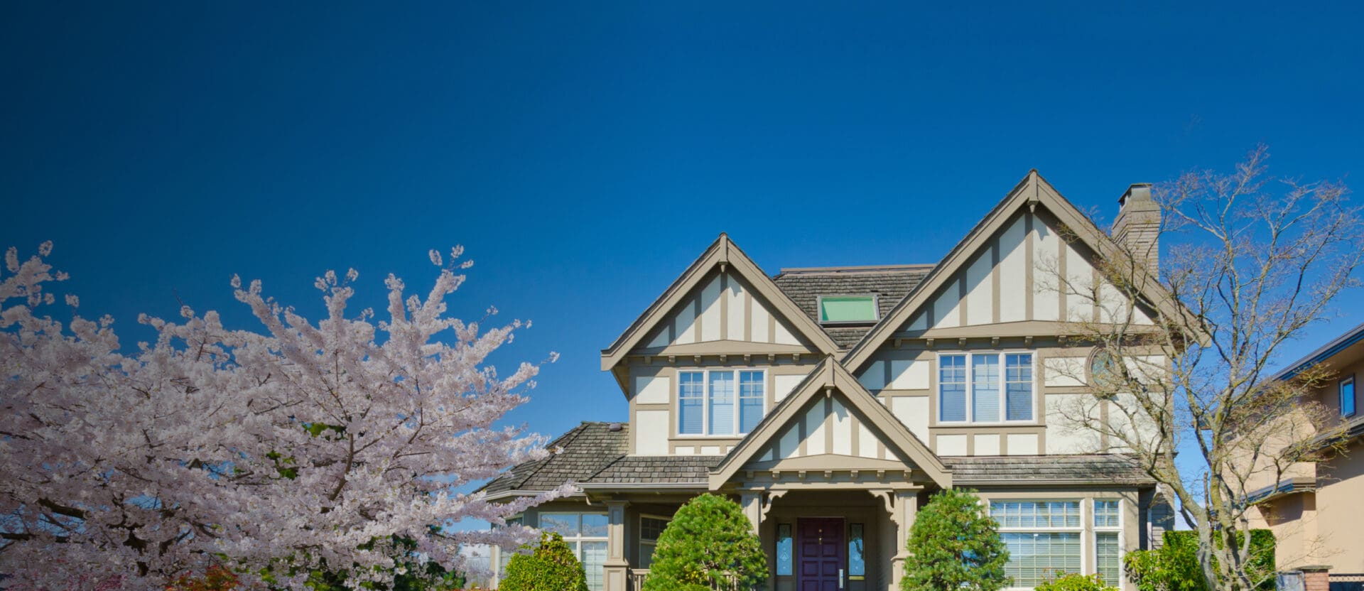 A house with a vibrant blue sky in the background and a blossoming cherry tree to the left, representing the spring season